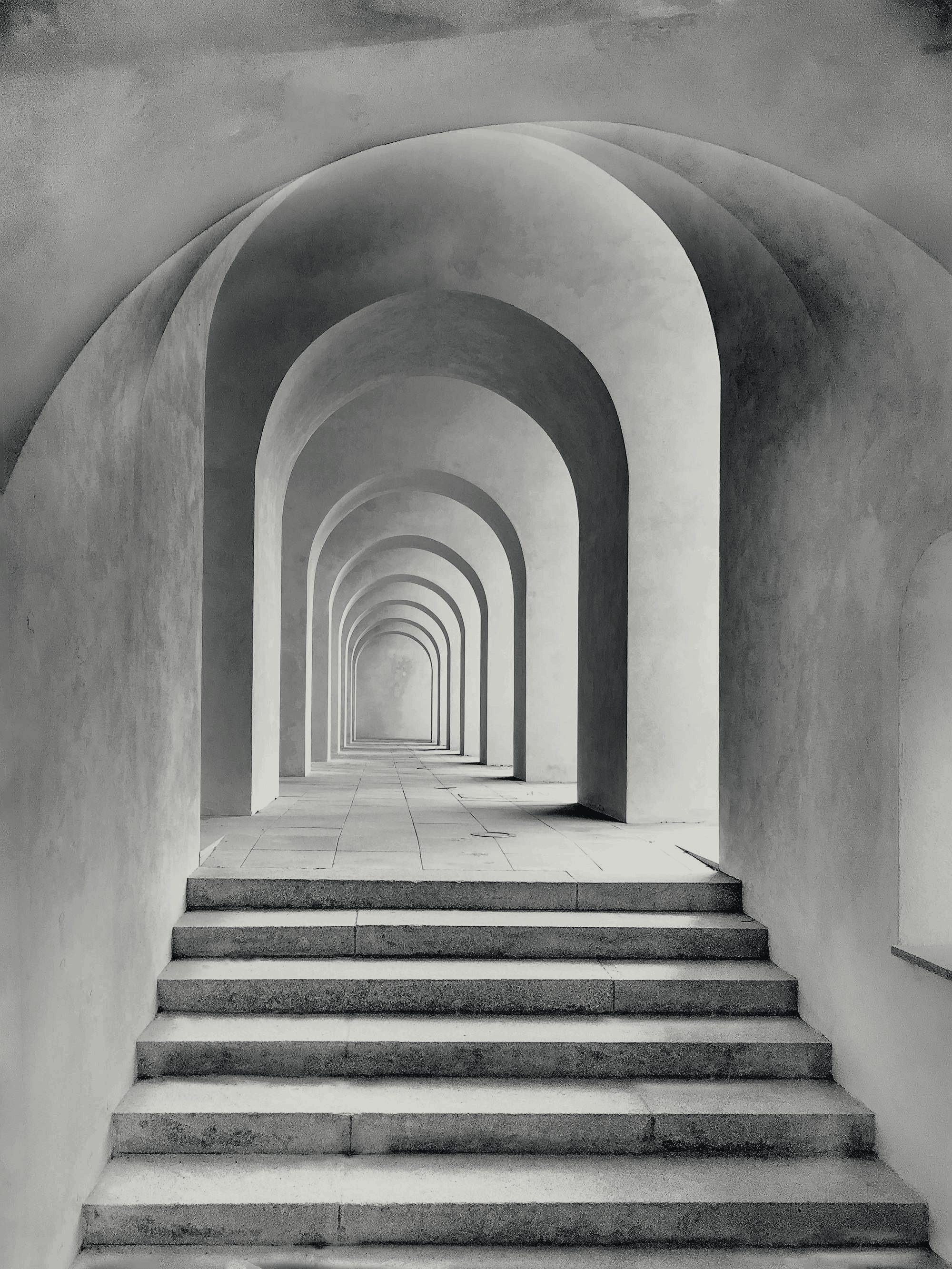 Um pórtico de arcos sucessivos, em concreto, com degraus que sobem em direção à luz.